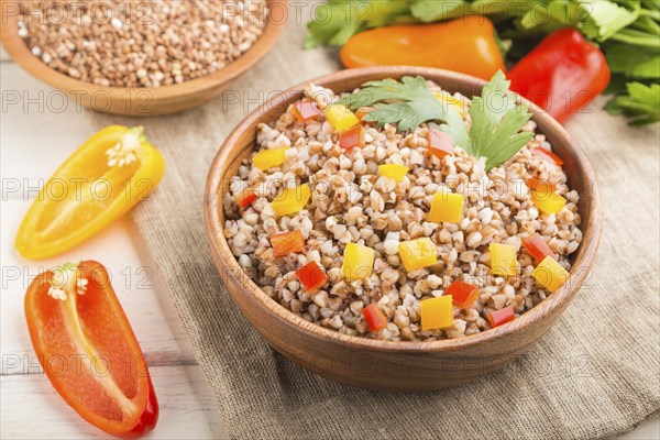 Buckwheat porridge with vegetables in wooden bowl on a white wooden background and linen textile.