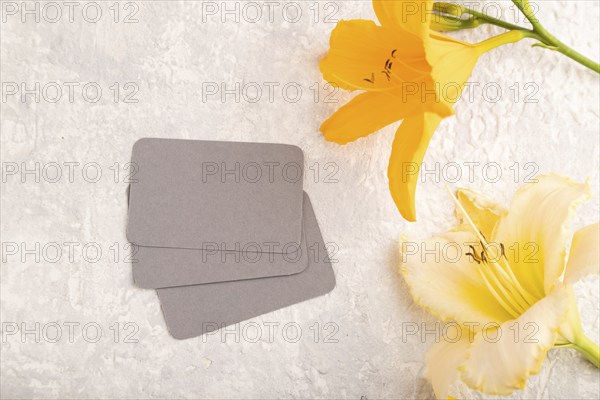 Gray paper business card mockup with orange day-lily flower on gray concrete background. Blank, top