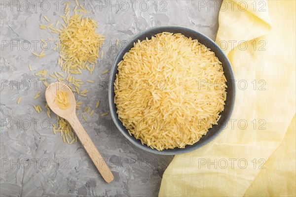 Blue ceramic bowl with raw golden rice and wooden spoon on a gray concrete background and yellow