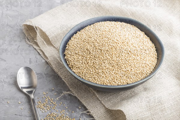 Blue ceramic bowl with raw white quinoa seeds on a gray concrete background and linen textile. Side