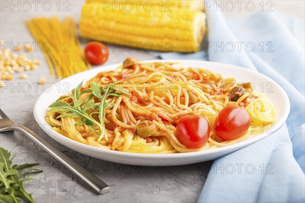 Corn noodles with tomato sauce and arugula on a gray concrete background and blue textile. Side