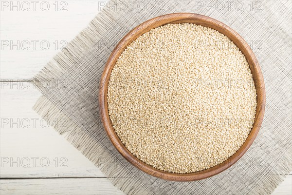 Wooden bowl with raw white quinoa seeds on a white wooden background and linen textile. Top view,