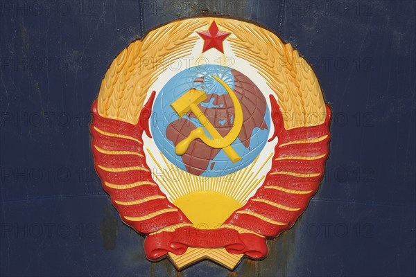 Soviet emblem featuring hammer and sickle over a globe, surrounded by wheat and topped with a red