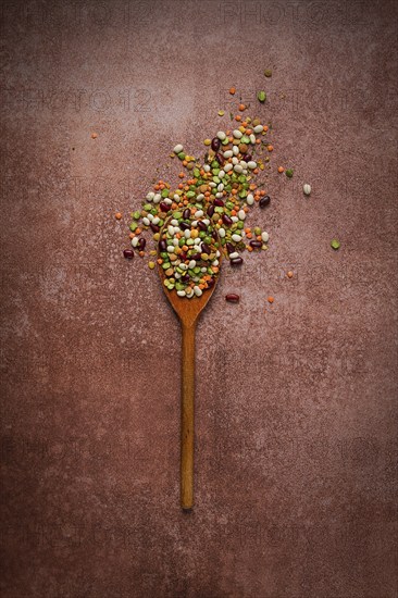 Wooden spoon, with an assortment of legumes, beans, peas, top view, on a brown background
