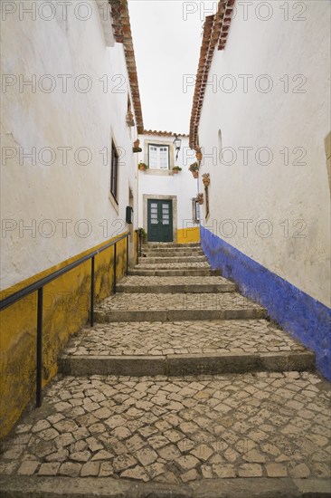 Old street with mosaic style paving stone stairs and white roughcast buildings with blue and yellow