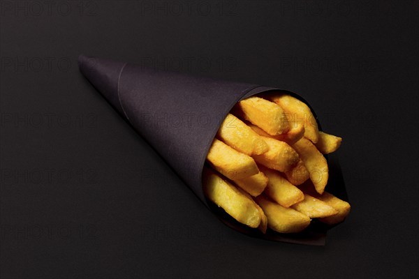 French fries, in black paper packaging, on a black background, close-up, selective focus