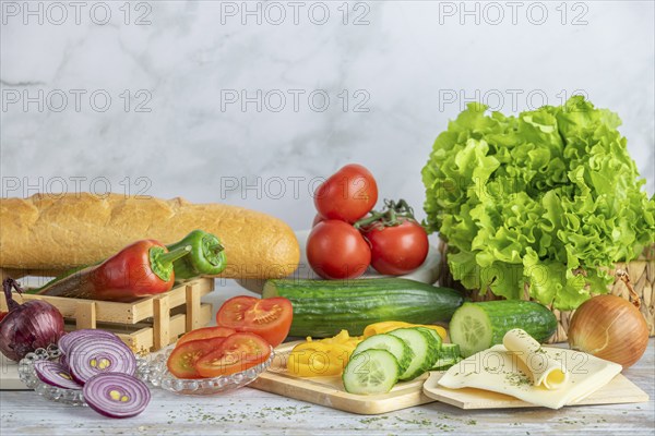 Colourful peppers, tomatoes and cucumber, some sliced, salad and cheese slices next to a baguette