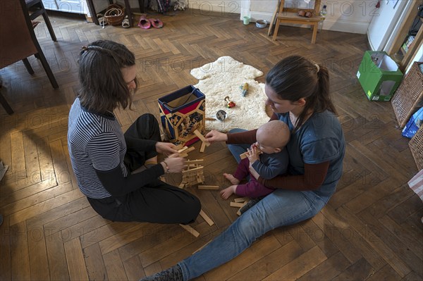 Young mother with her sister and with her son, 8 months, playing on the parquet floor,