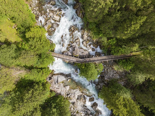 Aerial view of a wooden bridge over a raging river, surrounded by dense forest, Zillertal, Austria,