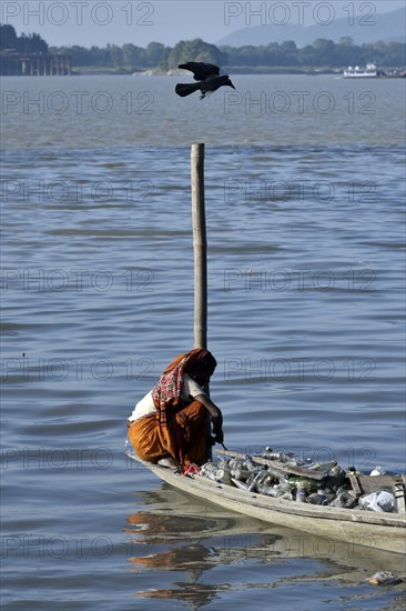 Rag picker collecting plastic bottle and other plastic materials in a boat from the bank of