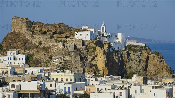 Panoramic view of a Mediterranean town with white buildings and a church on a rock, with the blue