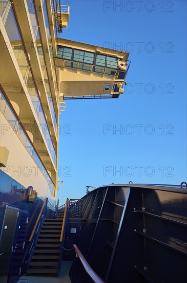 Modern cruise ship substructure with railings, windows and bridge under a bright blue sky with a