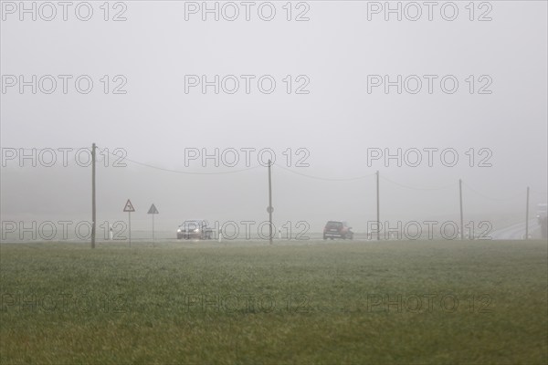 Cars drive over a country road with their lights on in dense fog, Neugarten, Brandenburg, 06.11