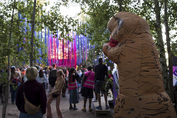 A festival visitor dressed as a dinosaur in front of a stage in the forest at the Melt Festival in