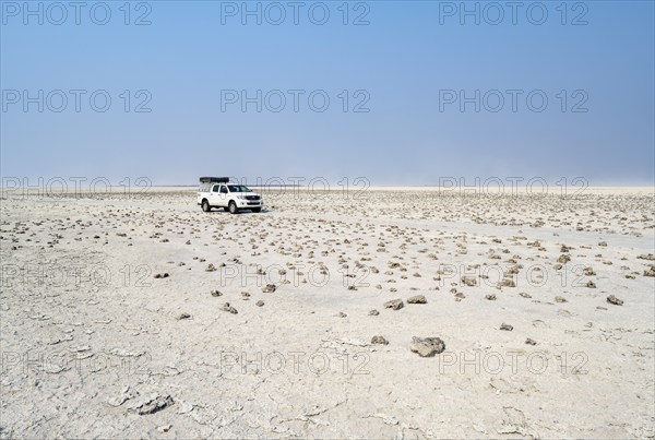 Four-wheel drive Toyota Hilux with roof tent, driving over salt pan, lone car in large wide plain,