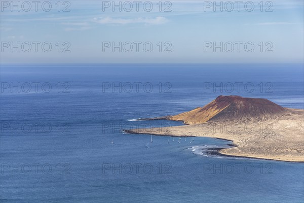 Landscape with island and volcanic crater on the coast and blue sea under clear sky, sailboats in