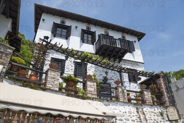 A traditional house with stone walls and balconies, surrounded by flowers under a clear blue sky,