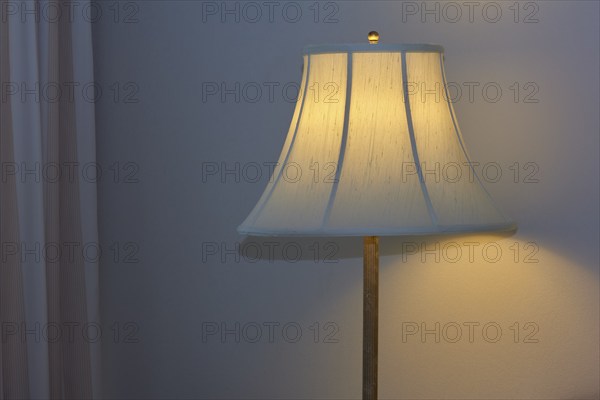 A warmly illuminated bedside lamp with a white shade, cosy
