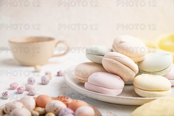 Colored zephyr or marshmallow with cup of coffee and dragees on white concrete background and