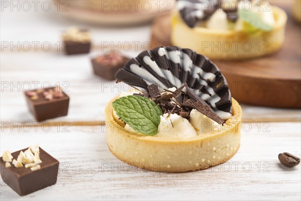Sweet tartlets with chocolate and cheese cream with cup of coffee on a white wooden background and