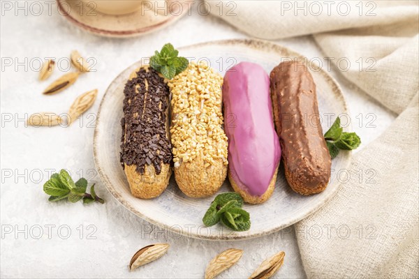 Set of eclair, traditional french dessert and cup of coffee on gray concrete background and linen