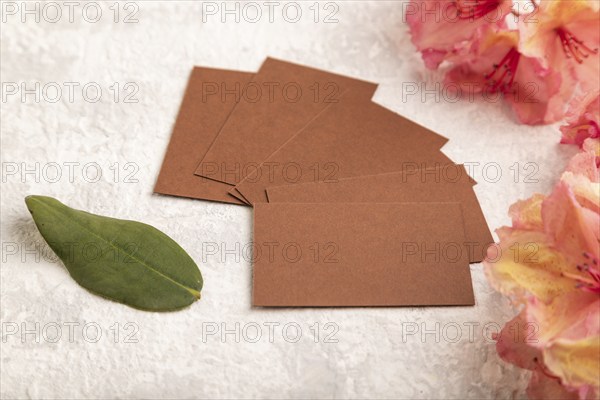 Brown business card with pink azalea flowers on gray concrete background. side view, copy space,