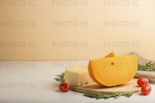 Various types of cheese with rosemary and tomatoes on wooden board on a white and orange background
