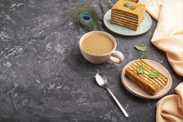 Homemade honey cake with milk cream and mint with cup of coffee on a black concrete background and