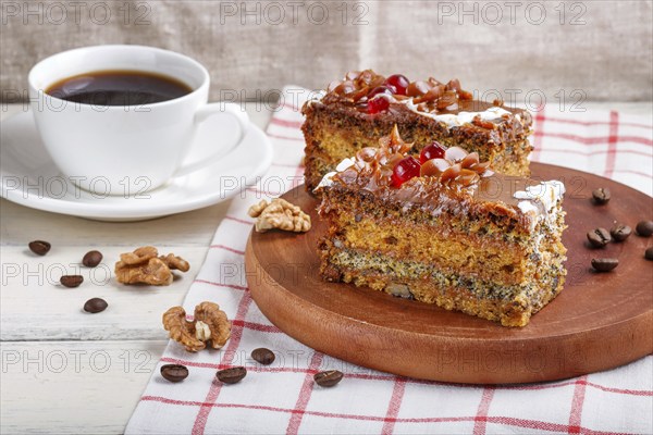 A piece of cake with caramel cream and poppy seeds on a wooden kitchen board and a cup of coffee,