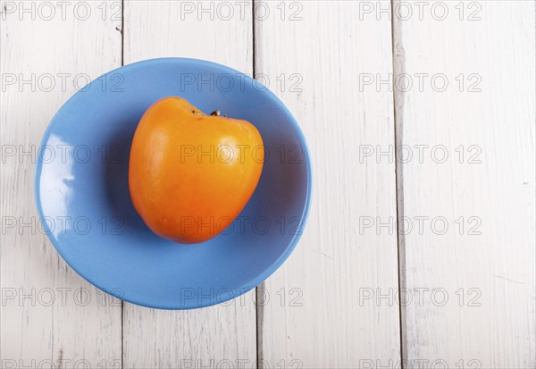 Ripe orange persimmon in a blue plate on white wooden background, with copy space