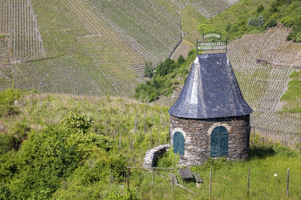 Stone hut with slate tower on a hill surrounded by green vineyards under a blue sky,