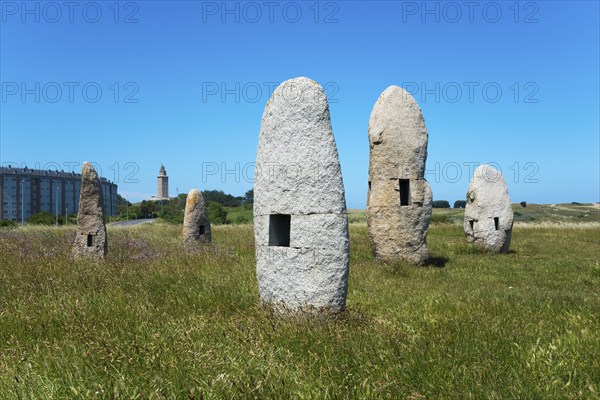 Stone formations in a meadow with a building in the background, under a clear blue sky, Menhires