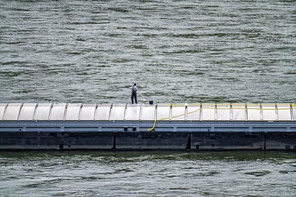 Inland waterway vessel, freighter, with closed cargo hatches, employee cleans the deck with water