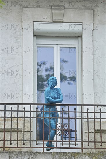 Sculpture by Nicole Brousse, blue woman on balcony railing in front of door, window, blue,