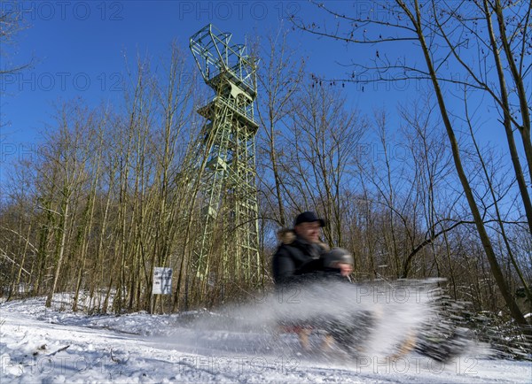 Winter in the Ruhr area, toboggan run on a forest path at Lake Baldeney, headframe of the former