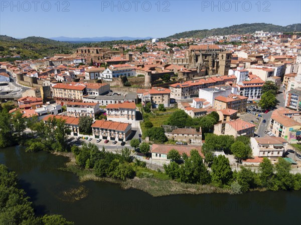 Historic city with red roofs and a dominant cathedral, surrounded by lush hills and a river in the