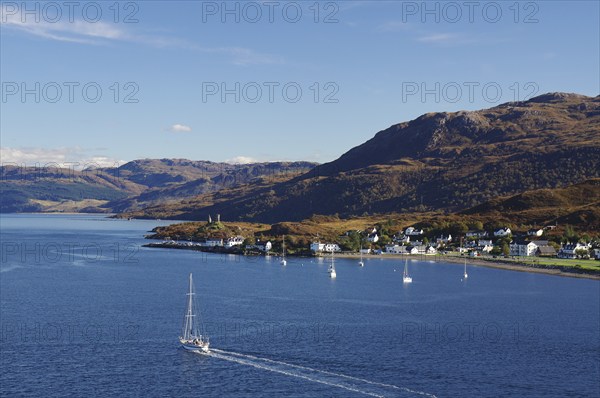 Coastal view with a sailing boat, village and hills in the background under a clear sky, autumn,