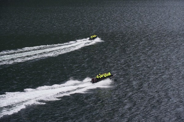Two speedboats with groups of people travelling fast in the Geiranger Fjord, white waves are coming