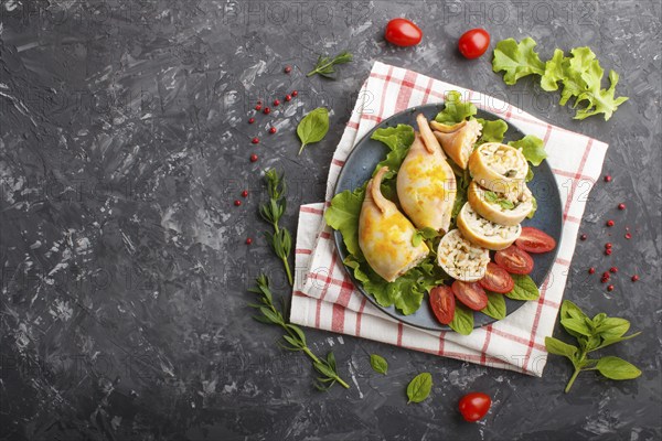 Stuffed baked squid with greens on a blue ceramic plate on a black concrete background, top view,