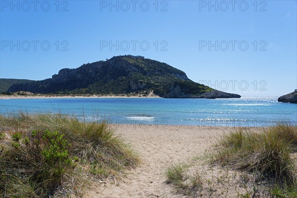 An idyllic beach with clear blue water and a mountain in the background on a sunny day, Voidokilia