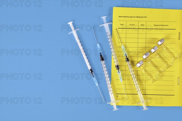 Vaccination concept with vaccine passport, 4 syringes and vials on blue background with copy space