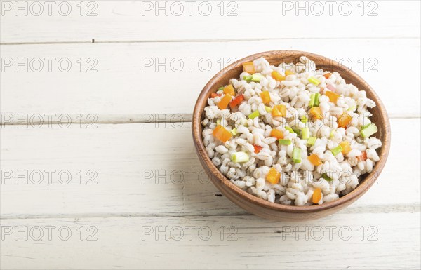 Pearl barley porridge with vegetables in wooden bowl on a white wooden background. Side view, copy