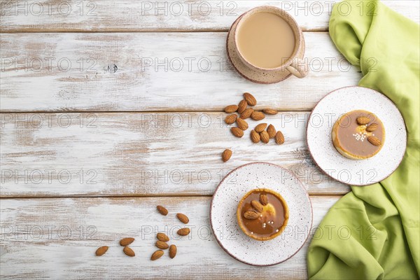 Sweet tartlets with almonds and caramel cream with cup of coffee on a white wooden background and