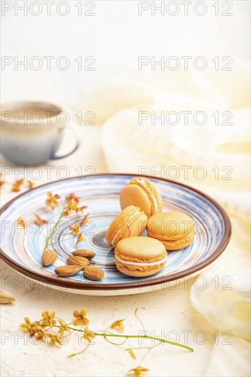 Orange macarons or macaroons cakes with cup of coffee on a white concrete background and linen