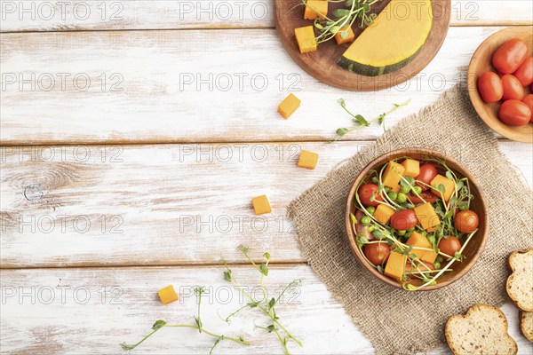 Vegetarian vegetable salad of tomatoes, pumpkin, microgreen pea sprouts on white wooden background