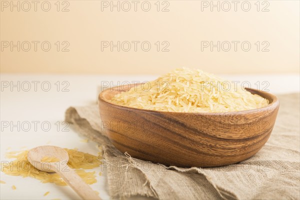 Wooden bowl with raw golden rice and wooden spoon on a white wooden background and linen textile.