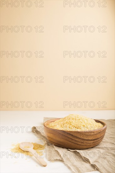 Wooden bowl with raw golden rice and wooden spoon on a white and orange background and linen