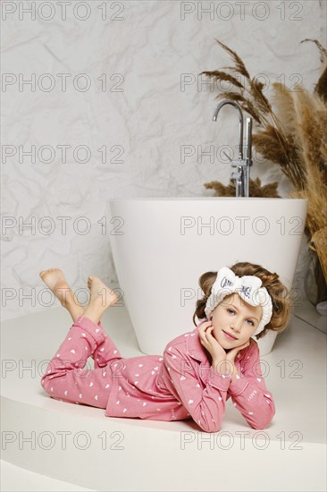 Smiling young girl laying down relaxed on the floor in the bathroom, wearing a cozy pink pajama and