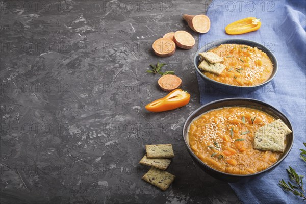 Sweet potato or batata cream soup with sesame seeds and snacks in blue ceramic bowls on a black