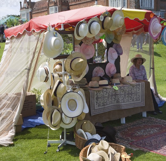 Woman selling hats from tent stall during garden event at Helmingham Hall, Suffolk, England, United